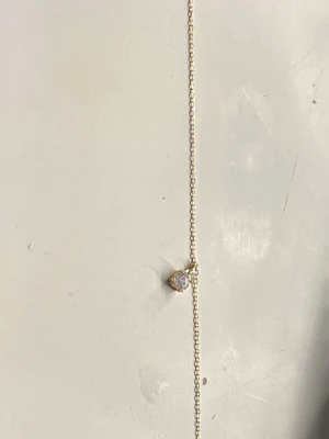 Guldhalsband med rund klar sten - Snyggt halsband i guld med en tunn kedja och ett hängsmycke med en rund, klar sten som gnistrar i ljuset. Enkel och stilren design som passar till många olika looks. Perfekt för dig som gillar minimalistiska smycken med en touch av elegans. Från glitter. Äkta guld