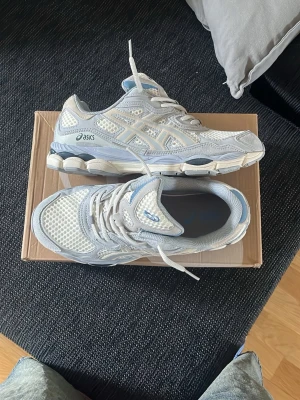 Vita och grå ASICS sneakers - Snygga sneakers från ASICS i vitt och ljusgrått med mesh- och syntetpaneler. Skorna har en chunky sula med grå detaljer och klassisk ASICS-logga på sidan. Perfekta för dig som gillar sportig och clean stil. liten i storlek 