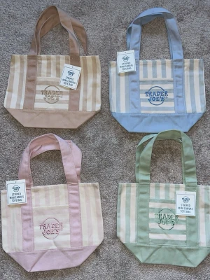 Randig minishoppingväska Trader Joe's - Säljer en randig minishoppingväska från Trader Joe's i canvas. Finns i flera färger: beige, blå och grön. Väskan har breda axelband, broderad logga på framsidan och praktisk ficka. Perfekt för att bära småsaker eller som accessoar. Denna annons står för den gröna väskan.💗