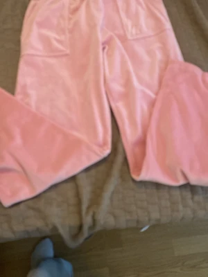 Rosa velourbyxor Juicy Couture - Säljer ett par klassiska rosa velourbyxor från Juicy Couture. Byxorna har bred resår i midjan och raka ben, perfekta för chill dagar hemma. Supermjukt material som känns lyxigt och bekvämt. Ikonisk loungewear som aldrig går ur tiden.