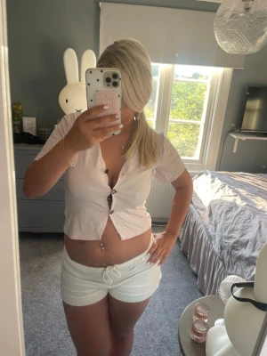 Vita shorts med snörning - Säljer en ljusrosa croppad topp med korta ärmar och v-ringning. Toppen har stora dekorativa knappar framtill och är tillverkad i ett mjukt, tunt material som passar perfekt till sommaren. Enkel och stilren design som är lätt att matcha. Köp och få med båda 