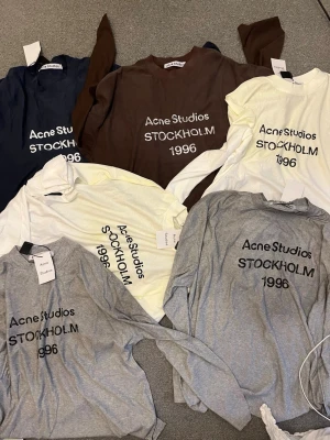Acne Studios långärmad t-shirt - Säljer flera långärmade t-shirts från Acne Studios med trycket 'STOCKHOLM 1996' på bröstet. Finns i färgerna grå, brun, vit, gul och marinblå. Perfekt för dig som gillar stilrena och trendiga plagg med enkel design.