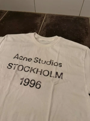 Vit acne tshirt S - Riktigt fet och eftertraktad t-shirt med acne studios loggan i storlek S. Väldigt bra skick! Obs: Jag är lite osäker på äktheten då lappen i nacken saknas, därför säljs den billigare (499 kr, nypris ca 3000 kr). längd cirka 65cm, bredd cirka 44cm. Tveka inte att höra av dig vid frågor eller funderingar!
