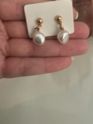 Guldiga örhängen med vita pärlor - Snygga örhängen med guldfärgade detaljer och droppformade vita pärlor. Klassisk design som ger en elegant touch till din stil. Perfekta för dig som gillar stilrena accessoarer med lite lyxig känsla.