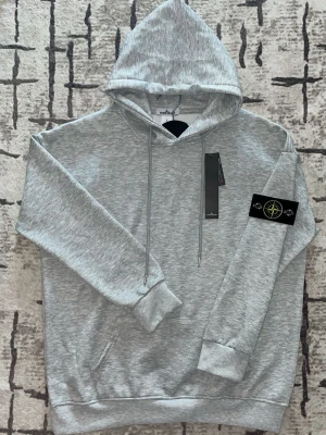 Stone Island hoodie - Säljer en grå Stone island hoodie i storlek L. Den passar skönt och är helt ny. Inte använt alls. Dropa vikt och längd så svarar jag om den passar. Är det något du undrar skriv!