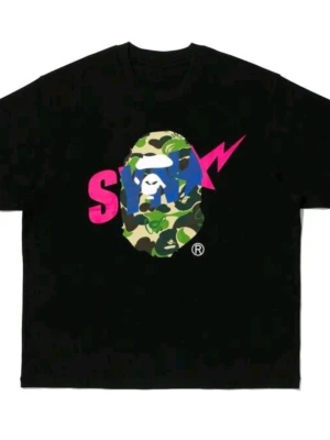 Svart bape t-shirt med camo och tryck - Säljer en svart t-shirt med ett stort färgglatt tryck på bröstet. Trycket består av ett kamouflagemönstrat ansikte, rosa bokstäver och en blå blixt. Klassisk passform och rund hals. Perfekt för dig som gillar streetwear och grafiska prints.