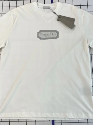 Vit t-shirt  - Säljer en stilren vit t-shirt från Christian med ett diskret tryck på bröstet. T-shirten har klassisk passform och rund halsringning. Perfekt för dig som gillar exklusiva och minimalistiska plagg.