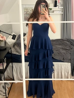 Marinblå balklänning  - Säljer en superfin marinblå bal/långklänning med flera lager av volanger och axelbandslös överdel. Klänningen är köpt från AW Bridal men då den inte satt som jag ville så säljer jag den. Helt ny och endast testad 1 gång, så i toppen skick helt utan defekter. 🥰 Byst=86.4cm	Midja=69.8cm	Höft=95.3cm	Håll till fåll=149.9cm🤗Jag är 176 cm lång och den går ner till marken. Tveka inte att fråga om du funderar över något🥰🤗