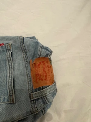 Ljusblå Levi's jeans straight fit - Säljer ett par klassiska ljusblå jeans från Levi's med rak passform. Jeansen har fem fickor, Levi's ikoniska läderpatch bak och röd logotagg vid bakfickan. Tillverkade i slitstark denim, perfekta för en avslappnad stil.. (lappen där bak är lite sönder, darför är priset som det är) Kan även förhandla om det är en snabb affär