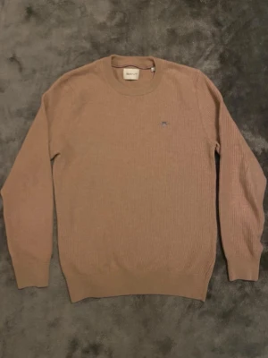 Beige stickad tröja från Gant - Säljer en stickad tröja i beige från Gant med rund halsringning och diskret logga broderad på bröstet. Den är i princip ny. Har dock inte kvar prislappen.