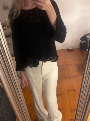 Svart virkad blus med vida ärmar - Svart blus i virkad stil med vida, långa ärmar och rund halsringning. Blusen har ett luftigt och löst fall, perfekt för en avslappnad look. Detaljerad virkning ger en bohemisk känsla.