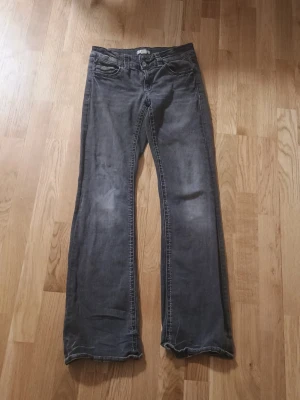 Grå bootcut jeans med slitningar - Säljer ett par grå bootcut jeans med snygga slitningar och kontrastsömmar. Jeansen har klassisk femficksmodell och normal midja. Perfekta för dig som gillar en avslappnad och trendig stil.