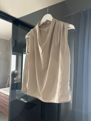 Beige ärmlös linnetopp - Snygg beige linnetopp med draperad halsringning och rak passform. Toppen är ärmlös och har en enkel, stilren look som passar till mycket. 