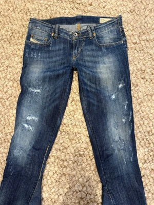 Blå bootcut jeans från Diesel - Snygga mörkblåa jeans från Diesel med slitna detaljer och tvättad look. Jeansen är bootcut och lågmidjade. De är utsydda och även förlängda, men inget man tänker på med dem på! Annars fint skick. Skriv vid frågor eller mått💕