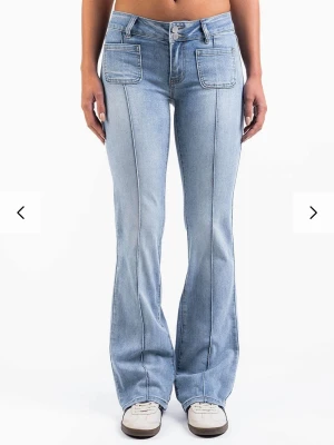 Ljusblå bootcut jeans med fickor - Snygga ljusblå bootcut jeans med markerade sömmar och stora framfickor. Jeansen har även fickor med knapp bak och är tillverkade i denim. Perfekt för dig som gillar en retrostil och vill ha ett par jeans som sticker ut. Jeansen är från madlady i storlek 34/tall, perfekt för dig med långa ben!
