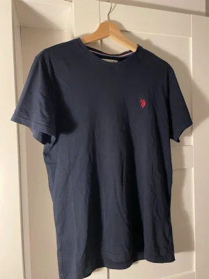 Mörkblå t-shirt från U.S. Polo Assn. - Snygg mörkblå t-shirt från U.S. Polo Assn. med klassisk passform och röd broderad logga på bröstet. Tröjan är oanvänd och priset är diskuterbart!