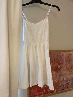 Vit somrig klänning med broderi - Söt vit klänning från H&M med tunna axelband och broderade detaljer på överdelen. Klänningen har en lätt utsvängd kjol och är gjord i ett tunt, luftigt tyg som passar perfekt för varma dagar. Enkel och stilren design med romantisk känsla.
