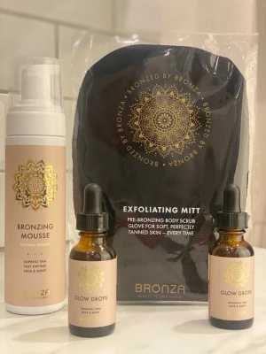 Bronza brun utan sol-kit - Komplett brun utan sol-kit från Bronza med bronzing mousse, glow drops och exfolieringsvante. Mousse och droppar ger en naturlig solbrun ton till ansikte och kropp. Förpackningarna är beige med gulddetaljer och svart vante. Perfekt för en jämn och fräsch bränna.