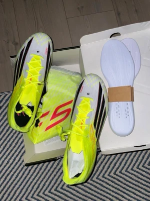 Adidas X Speedflow fotbollsskor gul - Säljer ett par Adidas X Speedflow fotbollsskor i neon-gult med svarta och röda detaljer. Skorna har en strömlinjeformad design, snörning och tillhörande innersulor. Ovandelen är i syntetmaterial för lätt vikt och bra bollkontroll. 