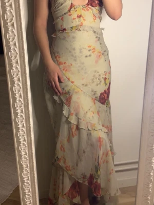 Lång blommig volangklänning - Klänningen har volangdetaljer och omlottkänsla, samt smala axelband. Perfekt för sommarens alla tillfällen.