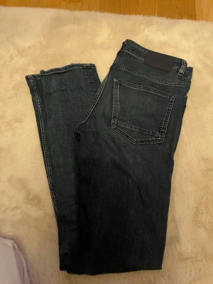 Mörkblå jeans från Selected Homme - Snygga mörkblå jeans från Selected Homme med klassisk femficksdesign och raka ben. Jeansen har diskreta slitningar och är tillverkade i bomull med lite stretch för extra komfort. Perfekta för en avslappnad och stilren look.