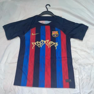 FC Barcelona Nike matchtröja randig - Snygg FC Barcelona matchtröja från Nike med klassiska blå och röda ränder, klubbmärke på bröstet och gul Nike-logga. Tillverkad i Dri-FIT-material som andas. Guldiga detaljer och sponsortryck både fram och bak. Perfekt för dig som älskar Barca och vill sticka ut på läktaren. Säljer den efter användning 3 gånger. Jag vill dock markera att den är klippt nedre kanten på tröjan , men annars är den i helt nytt skick.