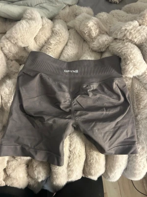 Grå bruna träningsshorts från DFYNE - Snygga grå cykelshorts från DFYNE med hög midja och seamless design. Stretchigt material och sitter helt perfekt. Använda typ en gång men tycker dom är lite för tajta typ för mig. Skulle säga de sitter som en xs. De vita texten har ju typ ramlat av men de är inte använda mer än en gång. Kostar 500kr nya. Kan skicka mer bilder eller så om de önskas💗