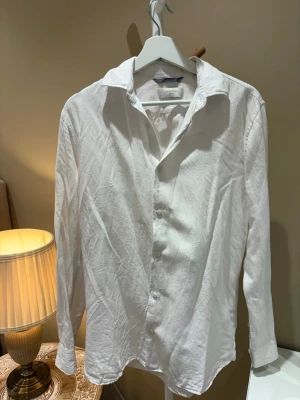 Vit linneskjorta från Jack & Jones - Säljer en klassisk vit skjorta från Jack & Jones i linne. Skjortan har lång ärm, knappar framtill och en avslappnad krage. Perfekt för dig som gillar en enkel och stilren look. Materialet är lätt och luftigt.