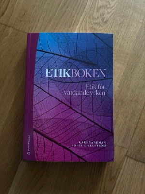 Etikboken: Etik för vårdande yrken - Etikboken: Etik för vårdande yrken av Lars Sandman och Sofia Kjellström. Boken är häftad och på svenska, utgiven 2024. Omslaget har ett färgstarkt mönster i blått, lila och rosa med bladstruktur. Perfekt som kurslitteratur för dig som pluggar till ett vårdyrke.