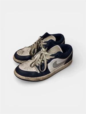 Nike Air Jordan 1 Low midnight navy  - Snygga Nike Air Jordan 1 Low midnight navy. Skorna har vita snören, perforerad tåbox och den ikoniska Swoosh-loggan på sidan. Tillverkade i läder med detaljer i textil och gummisula. Perfekta för dig som gillar streetwear. Storlek: 42