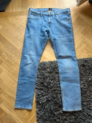 Ljusblå raka jeans från Lee - Säljer ett par klassiska ljusblå jeans från Lee med rak passform och fem fickor. Jeansen har en snygg tvätt och Lee-lapp bak i midjan. Tillverkade i slitstark denim med gul kontrastsöm. Perfekta för en avslappnad och trendig look.