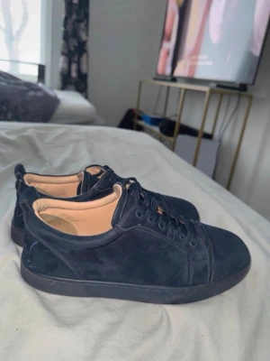 Mörkblåa sneakers från Louboutin - Snygga mörkblåa sneakers från Christian Louboutin i mocka med ton-i-ton snörning och diskret logga på hälen. Låg modell med klassisk siluett och beige innersula. Perfekta för dig som gillar stilrena och exklusiva skor.