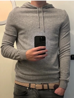 Soft Goat Hoodie - Mjuk och stilren grå stickad hoodie i 100% kashmir. Tröjan har dragsko i huvan, långa ärmar och ribbade muddar vid ärmslut och nederkant. Perfekt för dig som vill ha en lyxig och bekväm vardagslook. Tröjan är i storlek M men den sitter som en S 