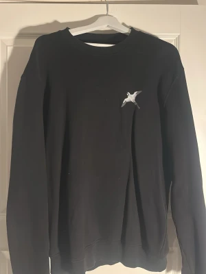 Svart sweatshirt från Axel Arigato - Stilren svart sweatshirt med rund hals och en liten broderad axel arigato fågeln på bröstet. Tröjan har ribbade muddar vid ärmslut och nederkant. Perfekt för en avslappnad och trendig look.