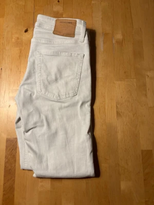 vita jeans 29/32 J&J - Snygga ljusgrå jeans från Jack & Jones med klassisk femficksdesign och rak passform. Tillverkade i mjukt denimtyg som ger en avslappnad look. Perfekta för dig som vill ha ett par stilrena och bekväma jeans.
