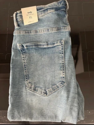 Ljusblå Molly jeans i storlek XL - Snygga ljusblå Molly jeans med hög midja och klassisk femficksmodell. Jeansen har en slim fit passform och är tillverkade i stretchigt denimtyg för extra komfort. Perfekta för dig som gillar en enkel och stilren look.