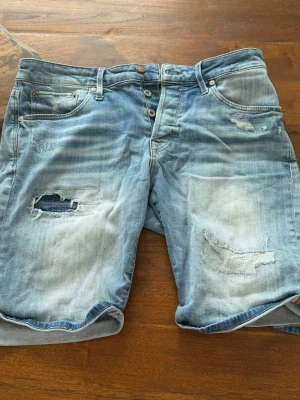 Blå slitna jeansshorts med hål - SÄLJER ETT TILL PAR FAST GRÅA, 1 PAR 149kr BÅDA 250KR!!! Säljer ett par blå jeansshorts med slitna detaljer och hål på båda benen. Shortsen har klassisk femficksdesign, knappar i gylfen och uppvikta benslut. Perfekta för en avslappnad och cool stil.
