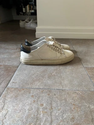 Vita sneakers från Axel Arigato - Stilrena vita sneakers från Axel Arigato med svart detalj på hälen. De är i storlek 39. Passar även 40