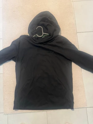 Svart hoodie från BOSS - Snygg svart hoodie från BOSS med minimalistisk logga på bröstet. Klassisk passform med huva och känguruficka framtill. Tillverkad i mjukt material som känns skönt mot huden. Perfekt för en avslappnad och stilren look.