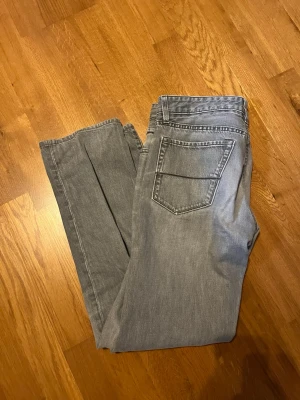 Ljusgrå jeans från Hugo Boss - Säljer ett par ljusgrå jeans från Hugo Boss med klassisk femficksdesign och en snygg detaljsöm på bakfickan. Jeansen har normal passform och är tillverkade i mjukt bomullstyg. Perfekta för dig som gillar en avslappnad men stilren look. I jeansen står det att storleken är W33 L34 men egentligen så är det som ett par W30 L32. Hör av dig om du har några funderingar!