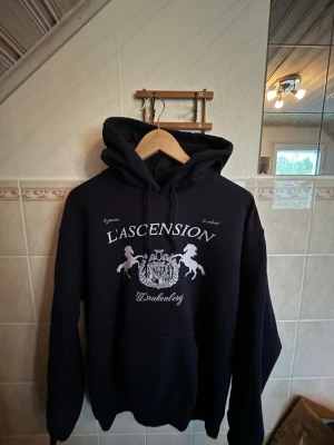Mörkblå hoodie från Drakenberg   - Snygg mörkblå hoodie med texten L'Ascension Drakenberg. Unikt tryck med lejon och sköld på bröstet. Perfekt nu till sommarens svalare sommarkvällar. Storleken är M men mer åt S, då jag själv är 186 lång och väger 72kg