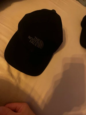 Svart keps från The North Face - Snygg svart keps från The North Face med böjd skärm och justerbar rem bak. Klassisk design med broderad logga framtill. Perfekt accessoar för en casual streetwear-look. Tillverkad i bomullsmix för skön passform.
