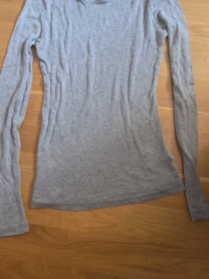 Grå långärmad topp från H&M - En enkel och stilren grå långärmad topp från H&M. Toppen har en rund halsringning och är figurnära i modellen. Perfekt att matcha med jeans eller kjol för en clean look.