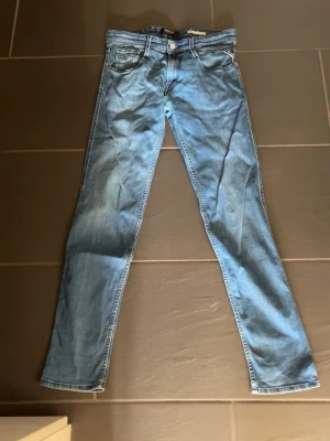 Ljusblå slim fit jeans från Replay - Snygga ljusblå slim fit jeans från Replay med klassisk femficksdesign och knappgylf. Jeansen har en smal passform och är tillverkade i mjukt denimtyg som ger en bekväm känsla. Perfekta för dig som gillar en stilren och modern look.