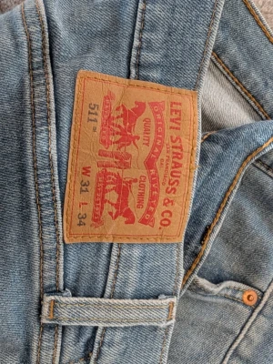 Levi's 511 ljusblå slim jeans - Säljer ett par Levi's 511 slim fit jeans i ljusblå denim. Klassisk femficksmodell med dragkedjegylf och snygga slitningar. Perfekta för dig som gillar en smalare passform och tidlös stil.