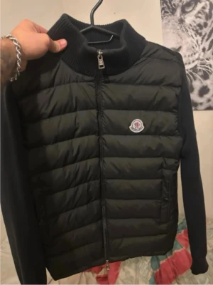 Moncler - Snygg svart dunväst från Moncler med quiltad front, ribbstickad krage och ärmar. Västen har dragkedja framtill och Moncler-logga på bröstet. Perfekt för lager-på-lager och streetstyle. Använd Moncler Cardigan. Pris kan diskuteras vid snabbaffär!