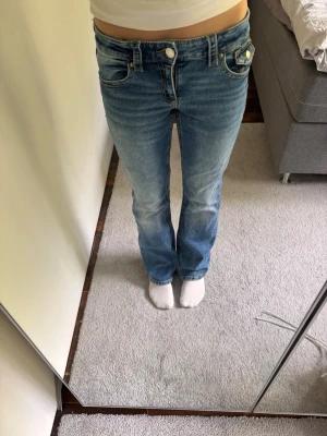 Blå bootcut jeans med låg midja - Snygga blå bootcut jeans med låg midja. Jeansen har slitningar framtill för en trendig look. Perfekta för dig som gillar en avslappnad men ändå stilren stil.