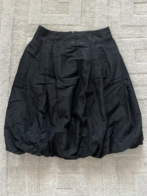Svart ballongkjol - Säljer en svart ballongkjol från Zara. Kjolen har en voluminös form och är tillverkad i ett glansigt material som ger en snygg look. Passar perfekt till en trendig outfit och har hällor för bälte i midjan.
