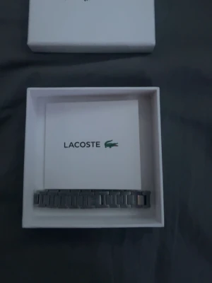 Silverfärgat armband från Lacoste - Snyggt armband från Lacoste i silverfärgad metall med stilren, länkad design. Kommer i originalförpackning och med en praktisk tygpåse. Perfekt accessoar för dig som gillar en clean och modern look.