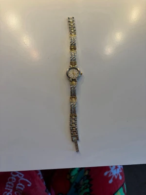 Silver och guld klocka - Stilren klocka i silver och guld med rund urtavla och länkarmband. Armbandet har ett tvinnat mönster och detaljer i både silver och guld, vilket ger en snygg kontrast. Perfekt accessoar för att lyfta din outfit.